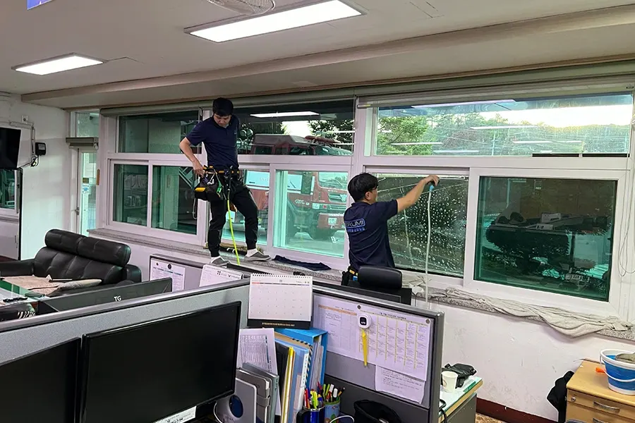 기술자 두 명이 사무실 창문에 필름을 부착하는 모습